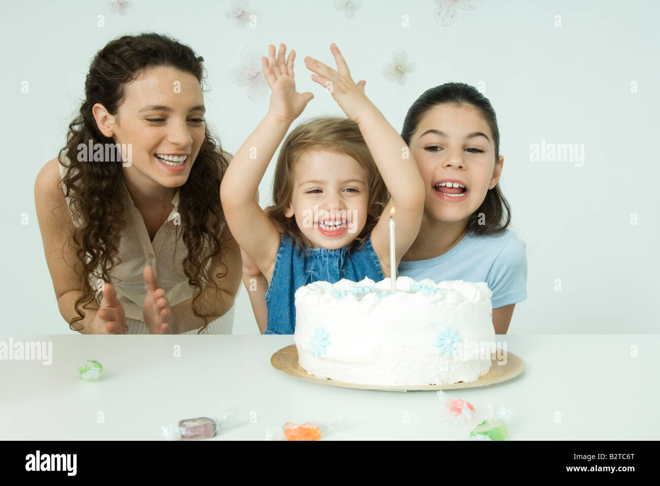 Girl cheering behind birthday cake, mother and sister watching ...