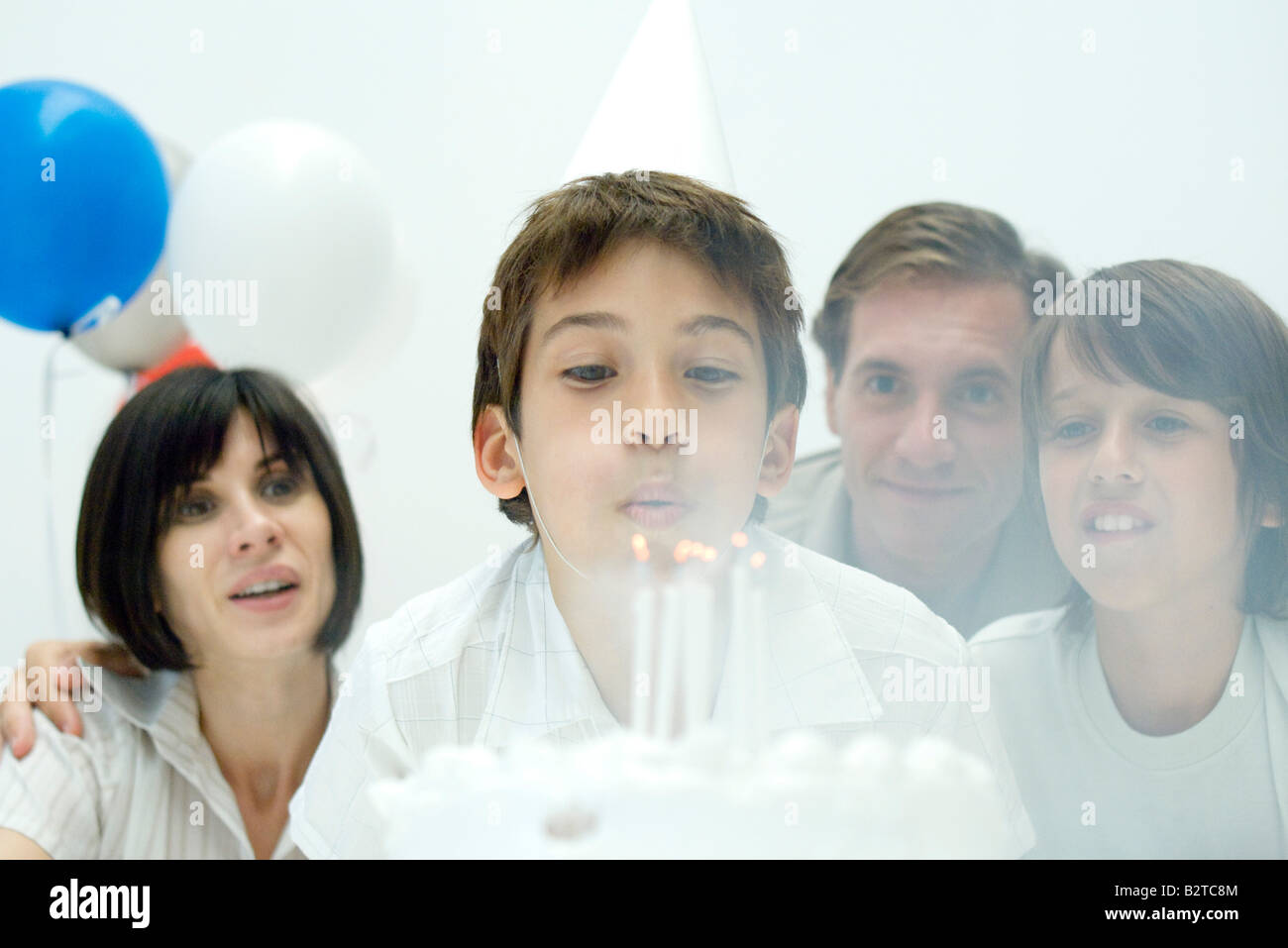 Boy blowing out candles on birthday cake, family watching Stock Photo