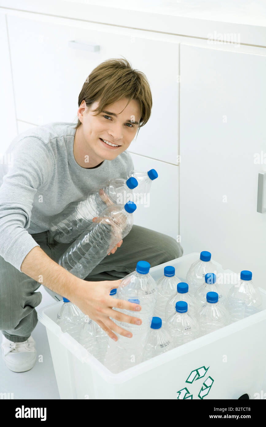Young man putting plastic bottles in recycling bin, smiling at camera