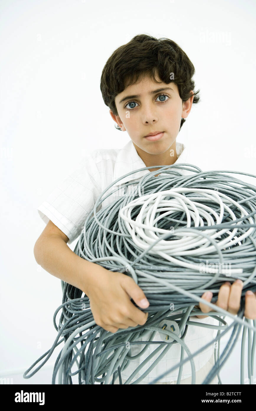Boy holding tangled electrical cords, looking at camera Stock Photo