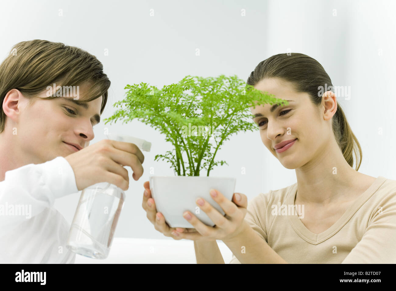Woman holding potted plant, man using spray bottle Stock Photo - Alamy