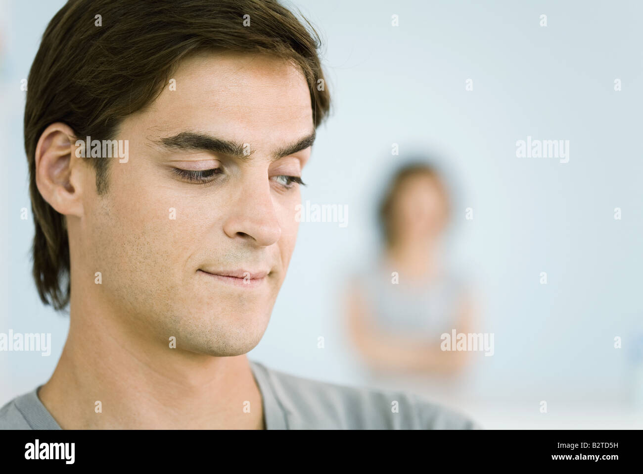 Man making sideways glance over shoulder, woman with arms folded in background Stock Photo