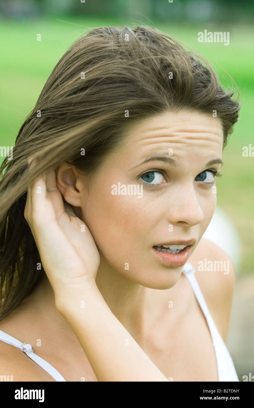 Teenage girl holding hand next to ear, looking sideways at camera, close-up Stock Photo
