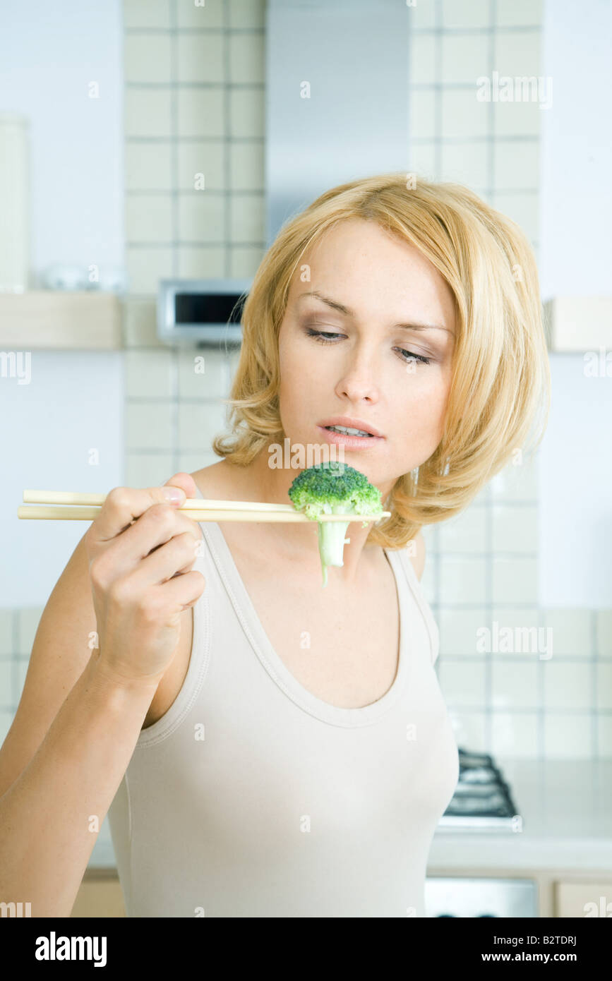 Woman holding broccoli with chopsticks, looking down Stock Photo