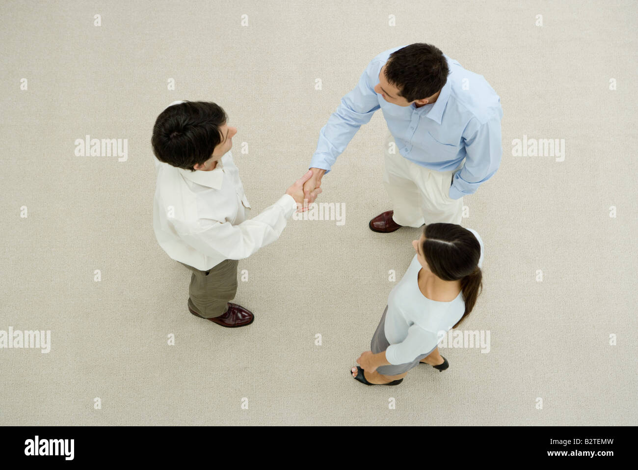 Two men shaking hands, female colleague watching, overhead view Stock Photo