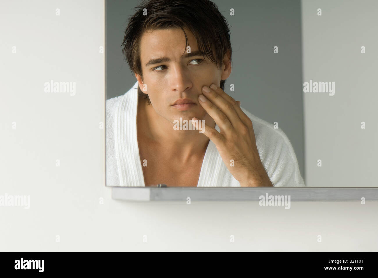 Man looking at self in mirror, touching cheek, cropped view of mirror Stock Photo