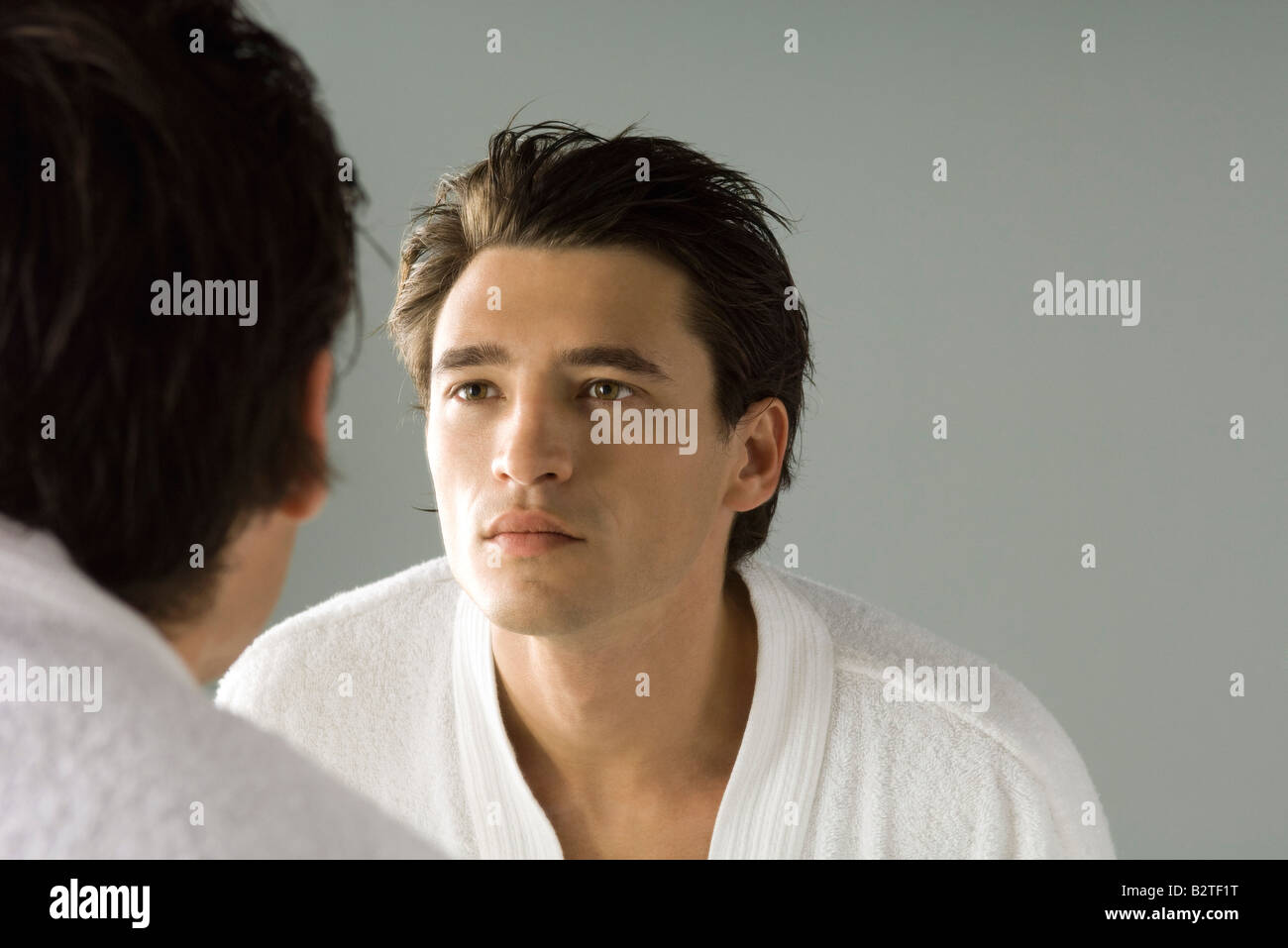 Man examining his face in the mirror, wearing bathrobe Stock Photo
