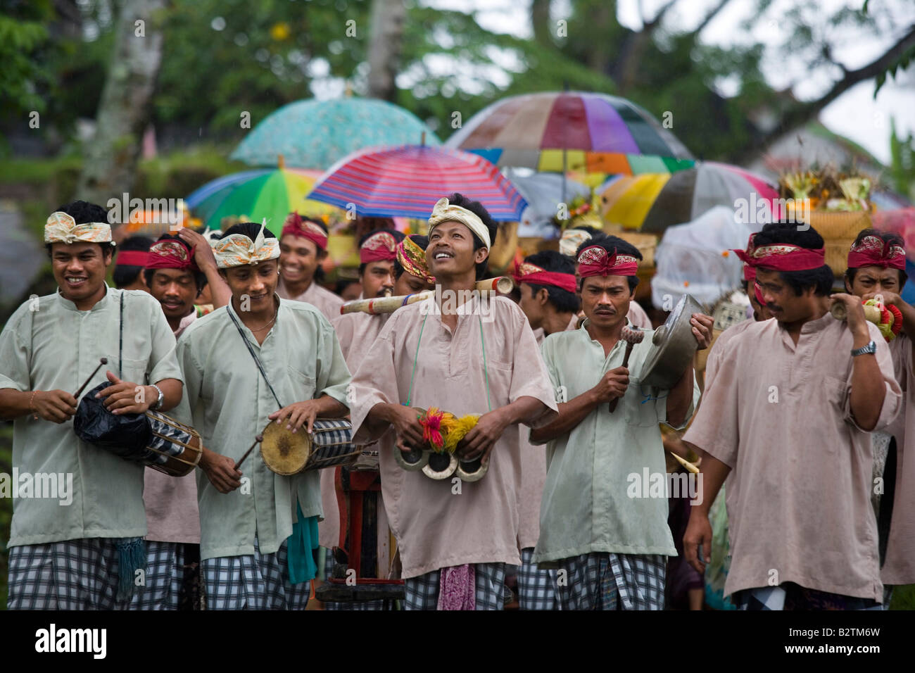 Procession of people walking down a wet road with the men at the front playing the drums in Bali Indonesia Stock Photo