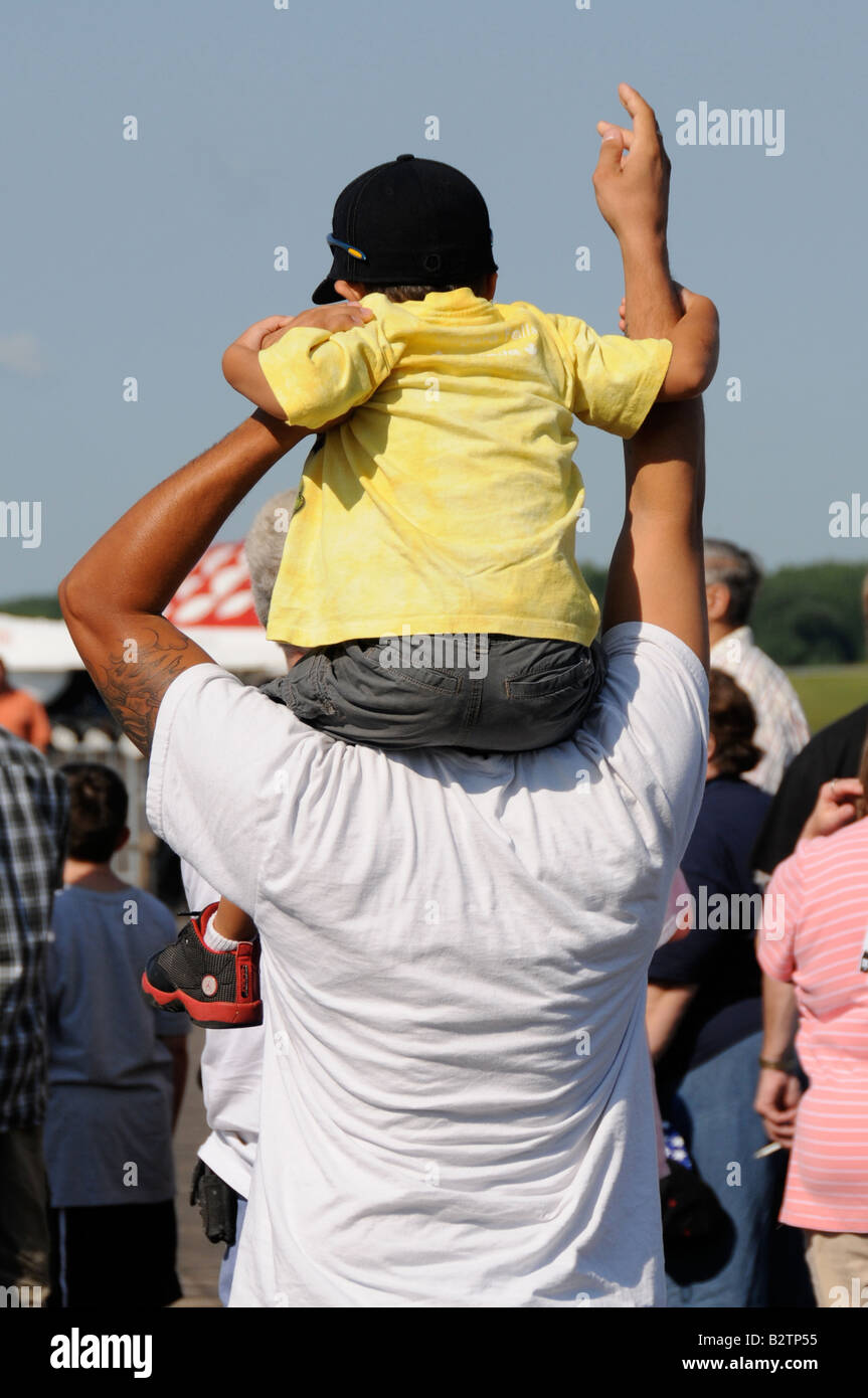 Young boy in yellow shirt sitting on fathers shoulder at airshow. Stock Photo