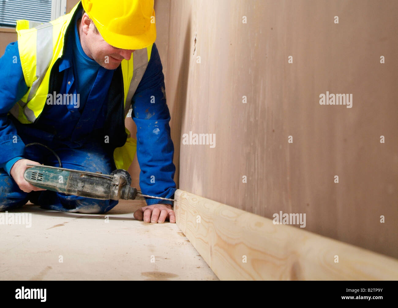 Man using an electric drill to fix skirting board to a wall Stock Photo