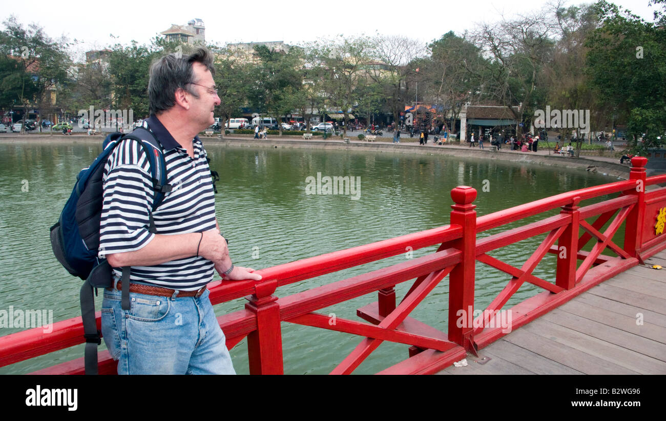 Tourist stands on the well known red Morning Sunlight or Huc Bridge at Hoan Kiem Lake Hanoi Vietnam Stock Photo