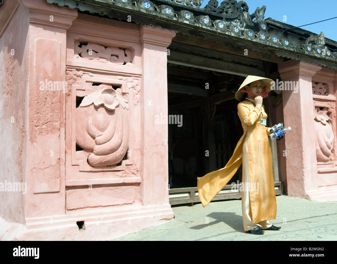 Conical hat in gold ao dai traditional costume landmark Japanese Covered Bridge Hoi An Vietnam Stock Photo