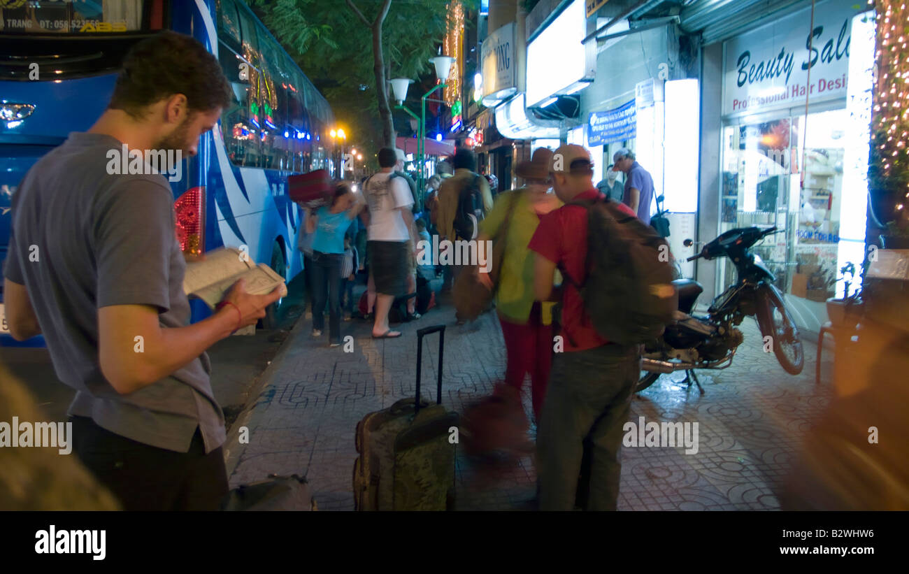 Young tourist consults travel guide at tour bus stop De Tham Street Ho Chi Minh City capital Vietnam Stock Photo