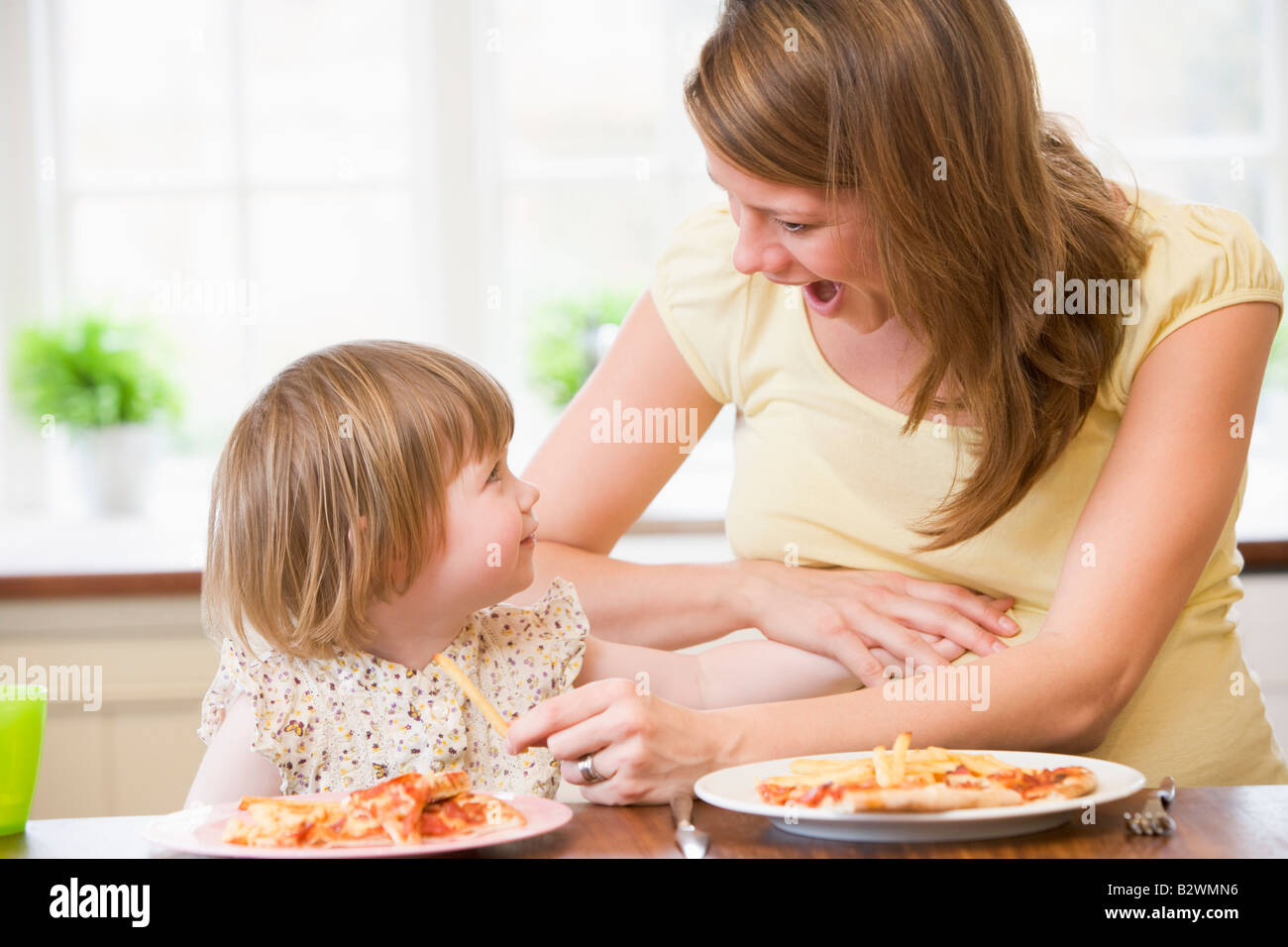 Pregnant mother with daughter touching belly eating French fries and pizza Stock Photo