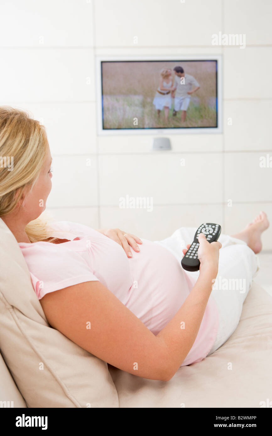 Pregnant woman watching television using remote control Stock Photo - Alamy