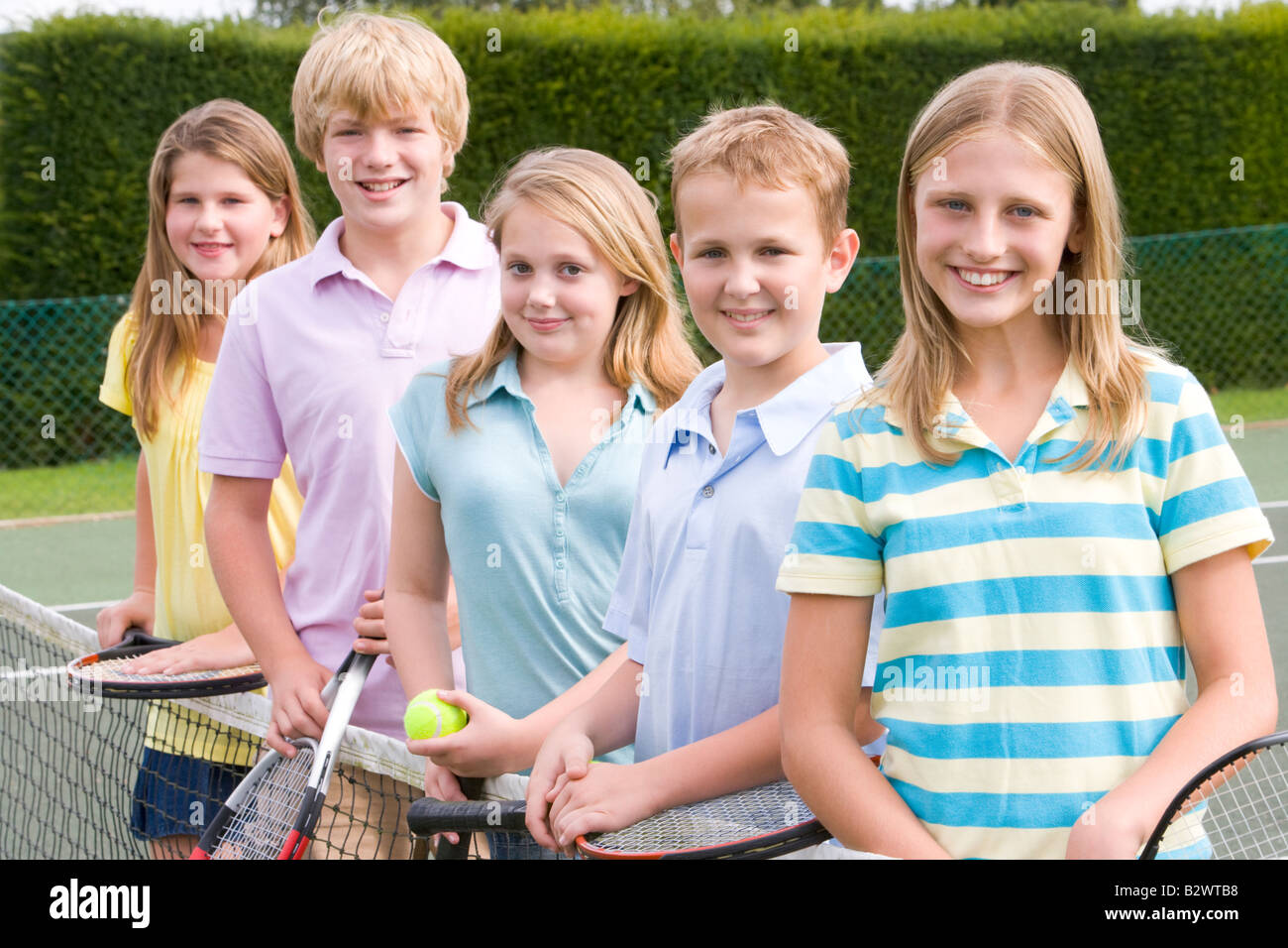 Five young friends with rackets on tennis court smiling Stock Photo
