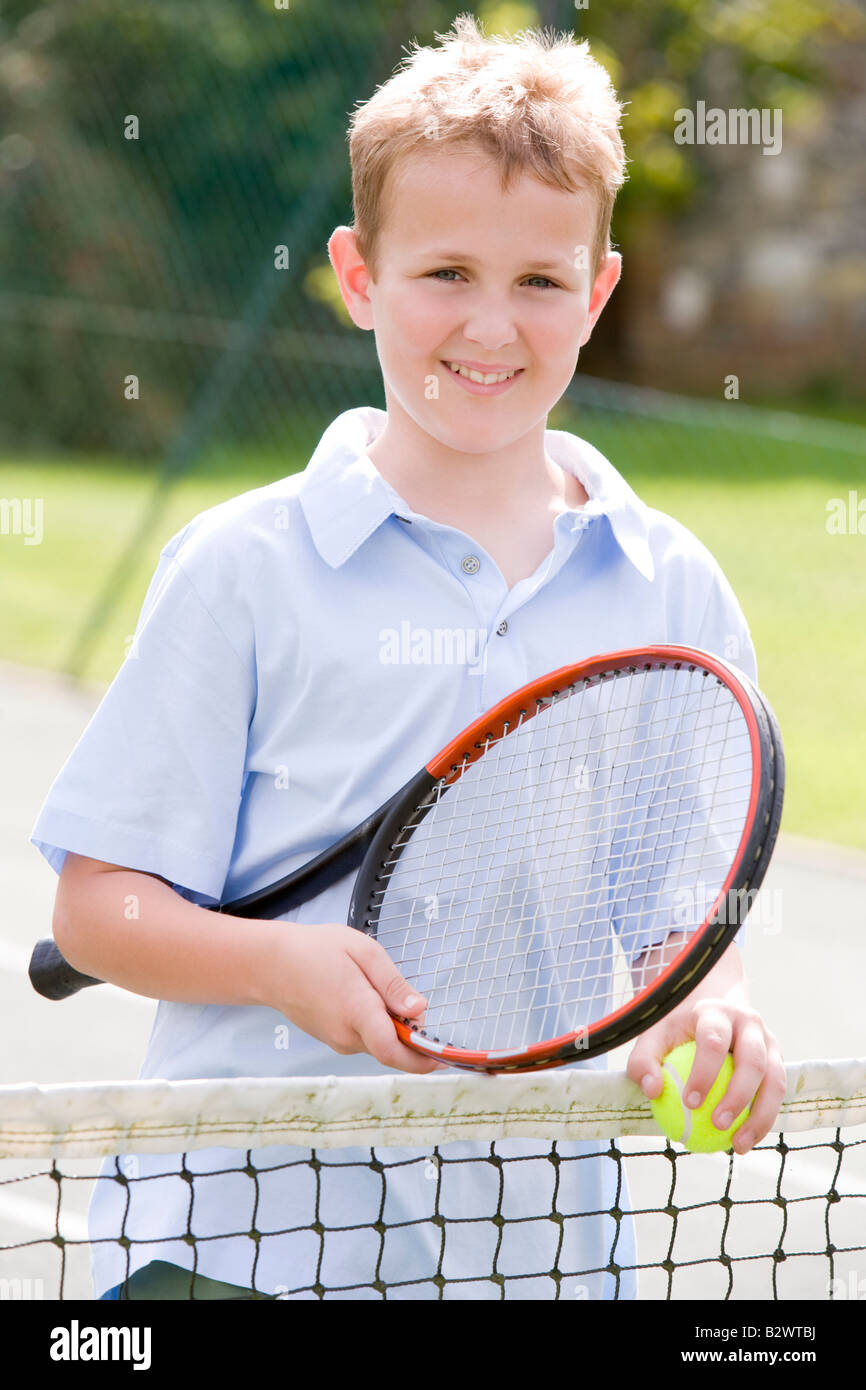 Young boy with racket on tennis court smiling Stock Photo