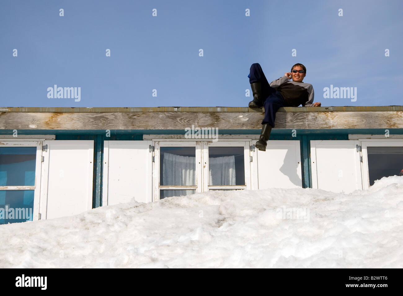A local Inuit man uses his mobile phone from his roof in the village of Ittoqqortoormiit, Scoresbysund, East Greenland Stock Photo