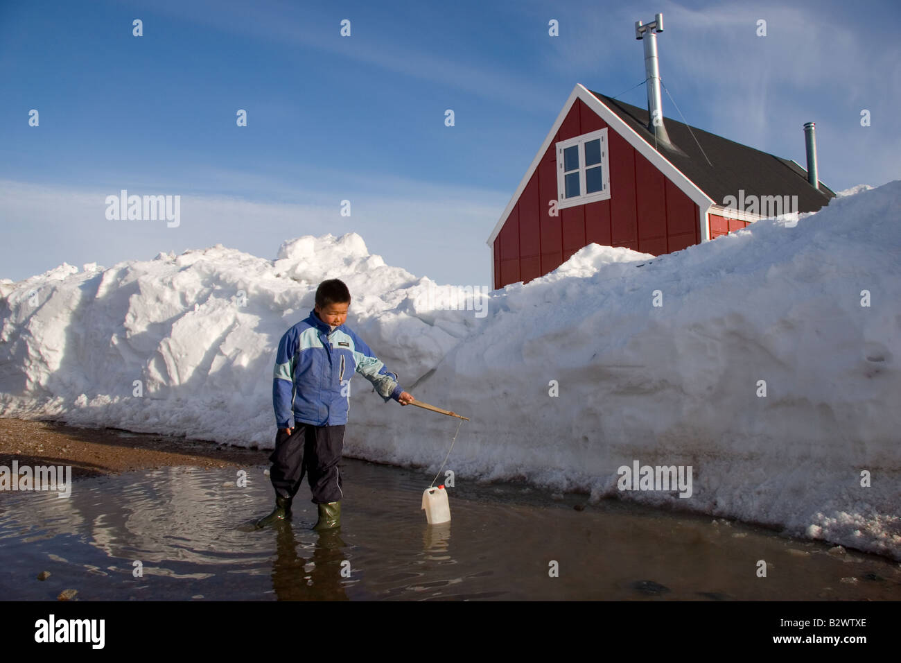 A young Inuit boy plays with an empty carton in a puddle in the village of Ittoqqortoormiit, Scoresbysund, East Greenland Stock Photo