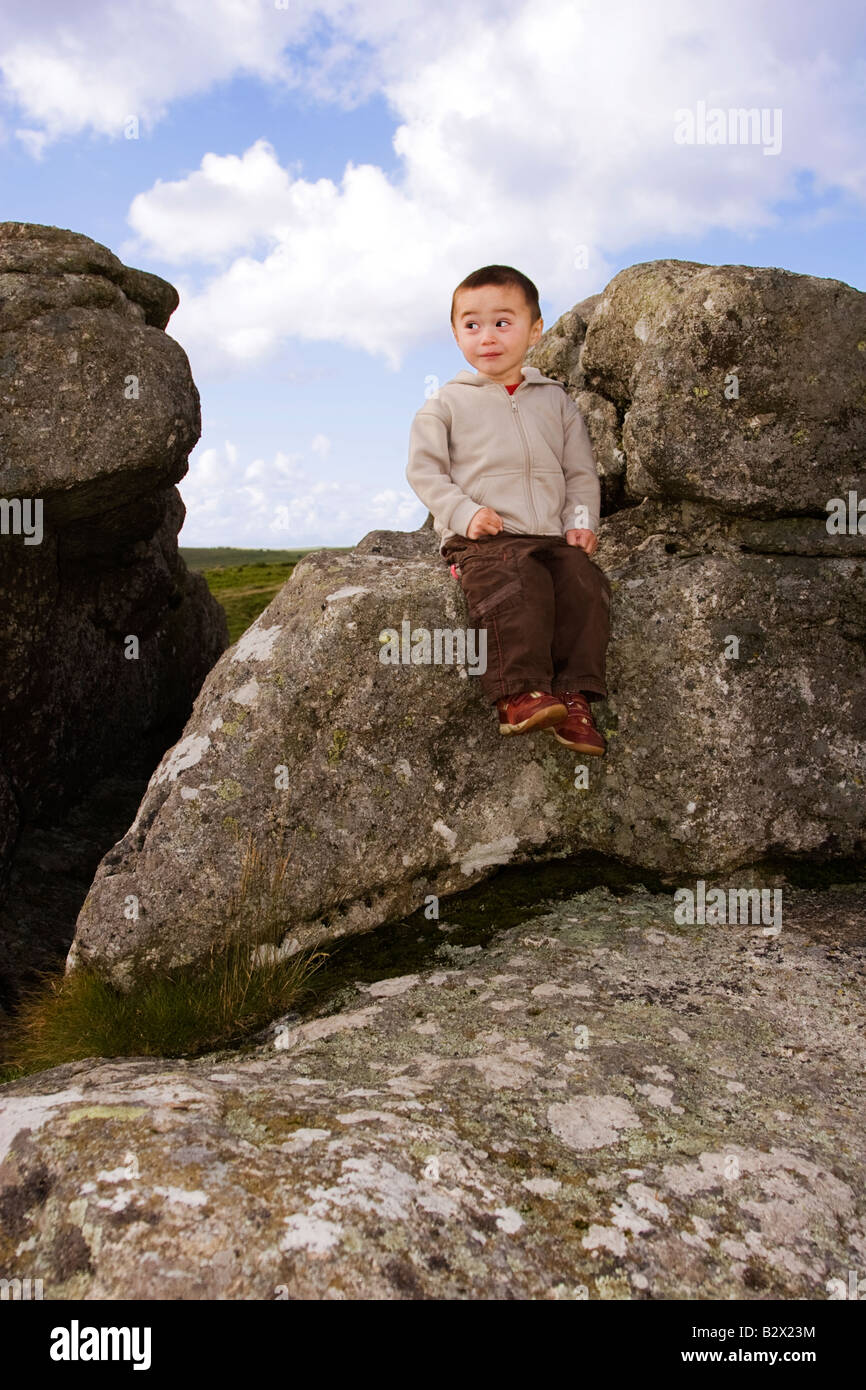Cheeky little boy with funny expression sitting on granite tor in Dartmoor National Park Stock Photo