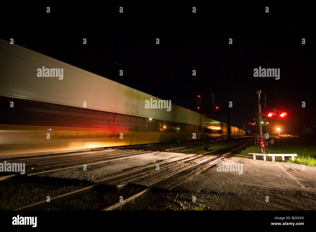 An intermodal train full of containers and trailers speeds past a crossing with waiting autos. Stock Photo