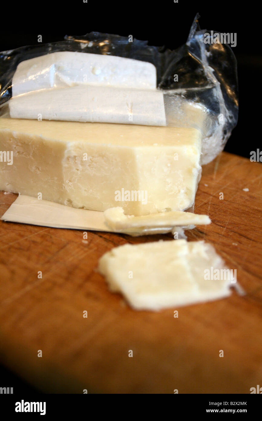 Artisan white cheddar cheese in wrapper on wood board. Stock Photo