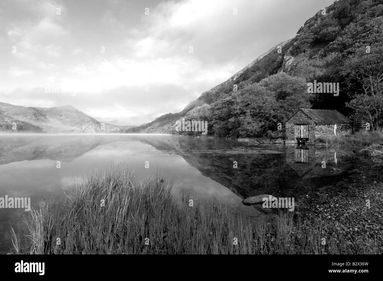 A small boathouse on a beautifully calm and misty morning at Llyn Dinas in Snowdonia national park North Wales in mono Stock Photo