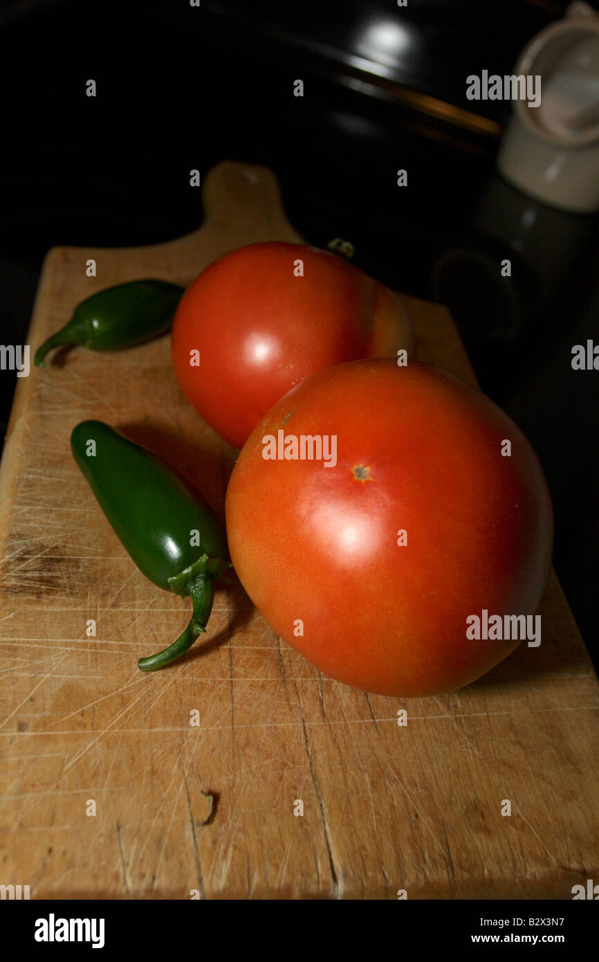 Two tomatoes and two jalapeño peppers on wood cutting board Stock Photo ...