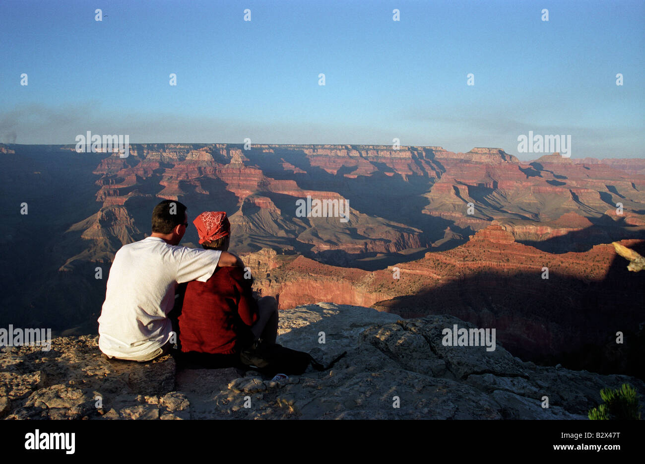 A man and a woman sit together at the edge of the Grand Canyon at ...