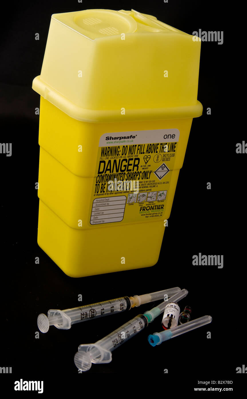 Hypodermic syringes and a broken ampoule beside a sharps box Stock