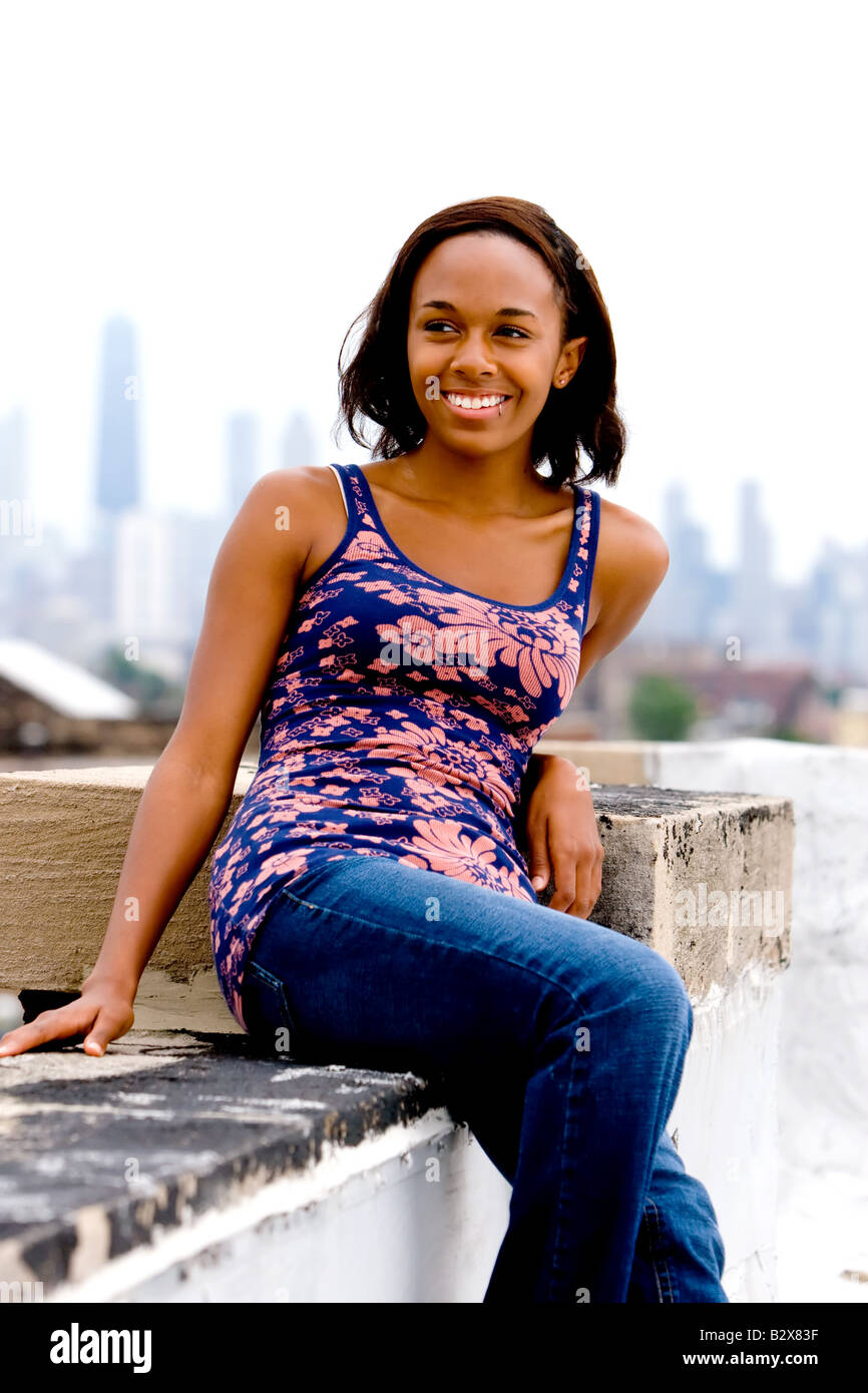 A young African American female hangs out on the roof of an urban building, observing the city below. Stock Photo