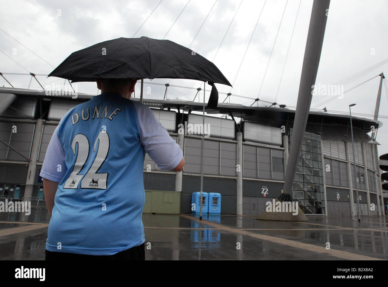 Fan outside City of Manchester Stadium Manchester City F.C holding umbrella Stock Photo