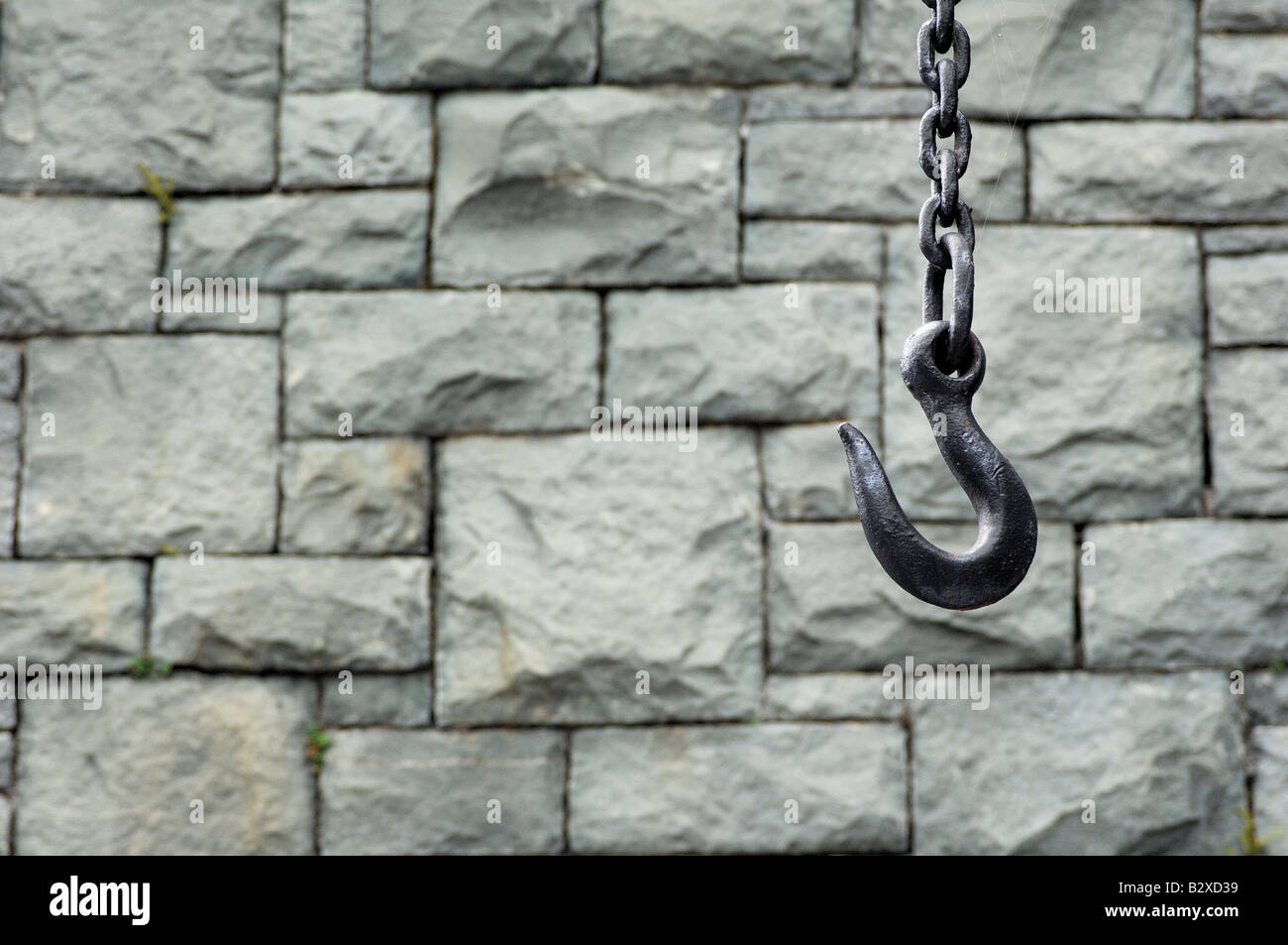 A large metal hook on a thick chain hanging in front of a slate wall