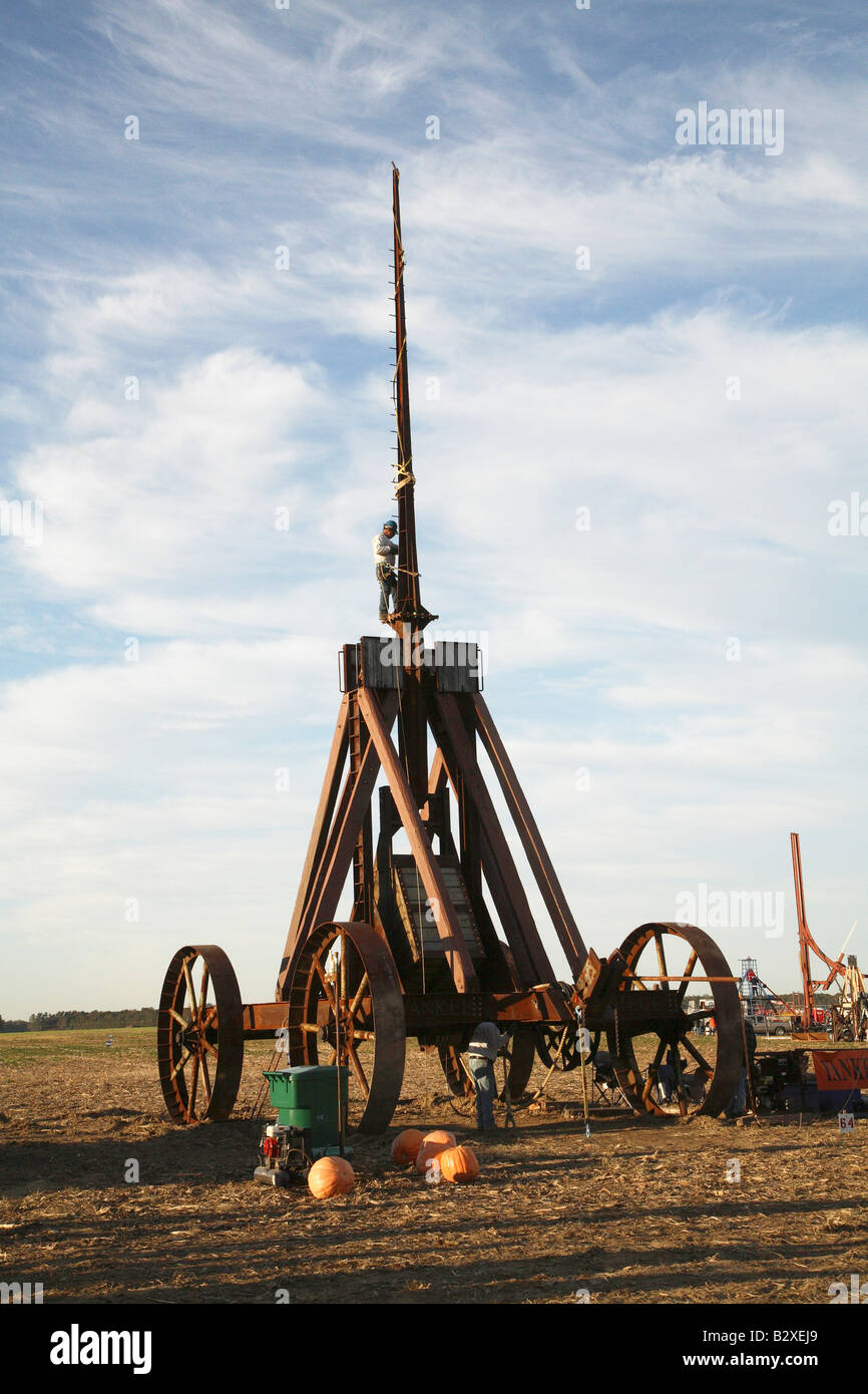 Huge iron wheeled Yankee Siege Trebuchet with person standing on tiny ledge at bottom of tall arm secured with safty rope. Stock Photo