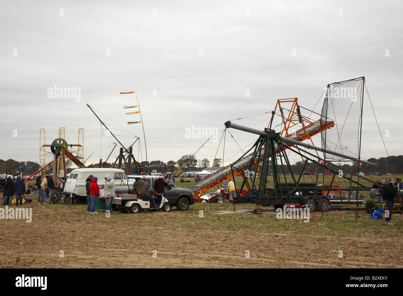 Assortment of catapults and human powered machines line the side of competition field along with support vehicles and owners Stock Photo