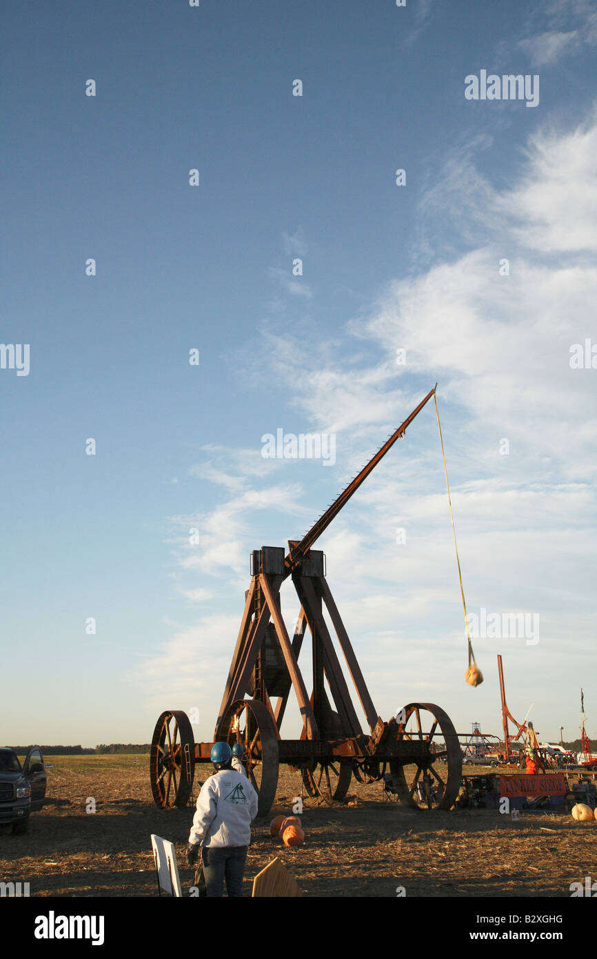 Huge iron wheeled Yankee Siege Trebuchet with fling arm rising towards vertical and pumpkin in sling rising behind it Stock Photo