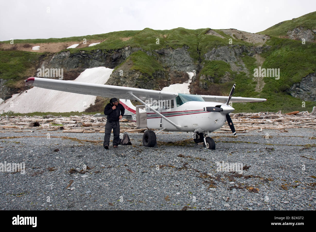 Pilot inspecting his airplane before taking of from a beach covered with driftwood in Katmai, Alaska Stock Photo