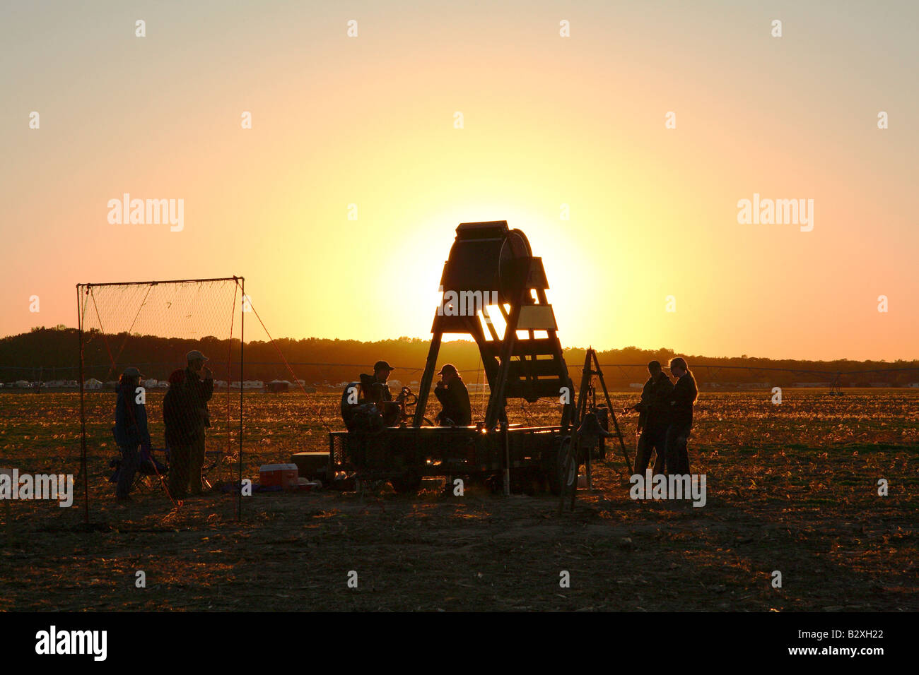 Wooden barrel shaped human powered pumpkin flinging machine with glow of setting sun directly behind Stock Photo
