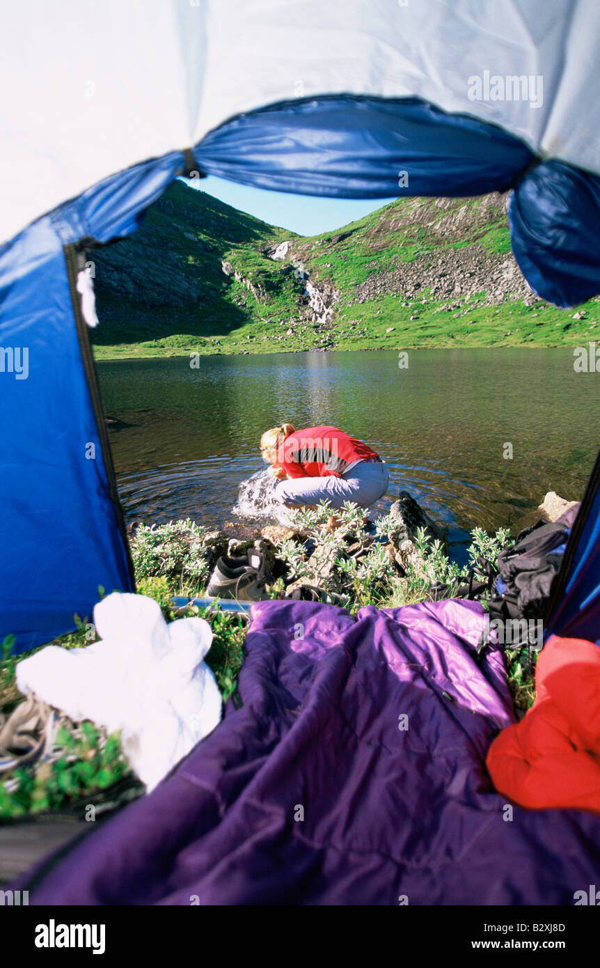Woman outdoors at campsite by tent splashing water from river on face Stock Photo