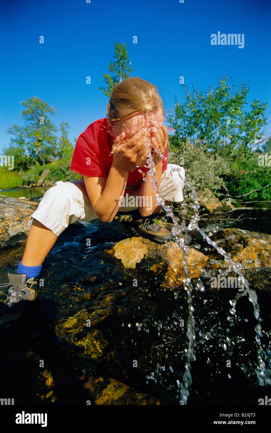 Woman outdoors by a lake splashing water on face Stock Photo