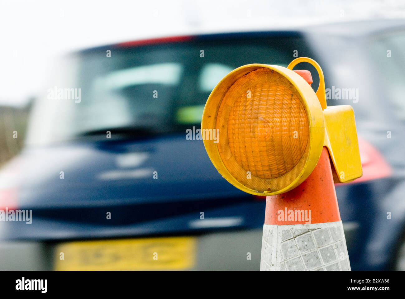 Car passing a yellow flashing light on top of a cone in roadworks in
