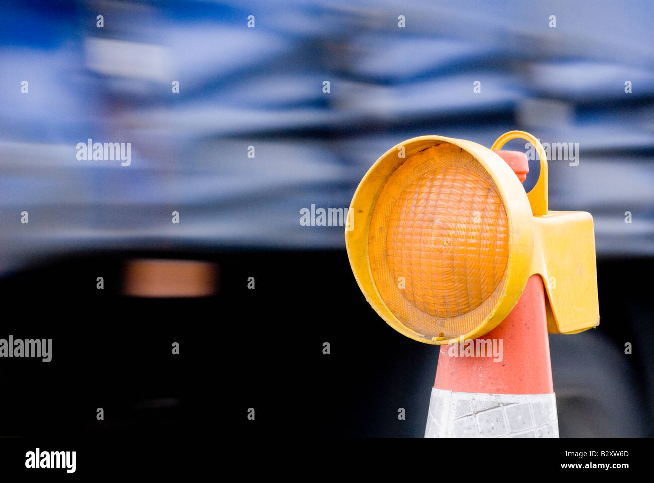 Car passing a yellow flashing light on top of a cone in roadworks in