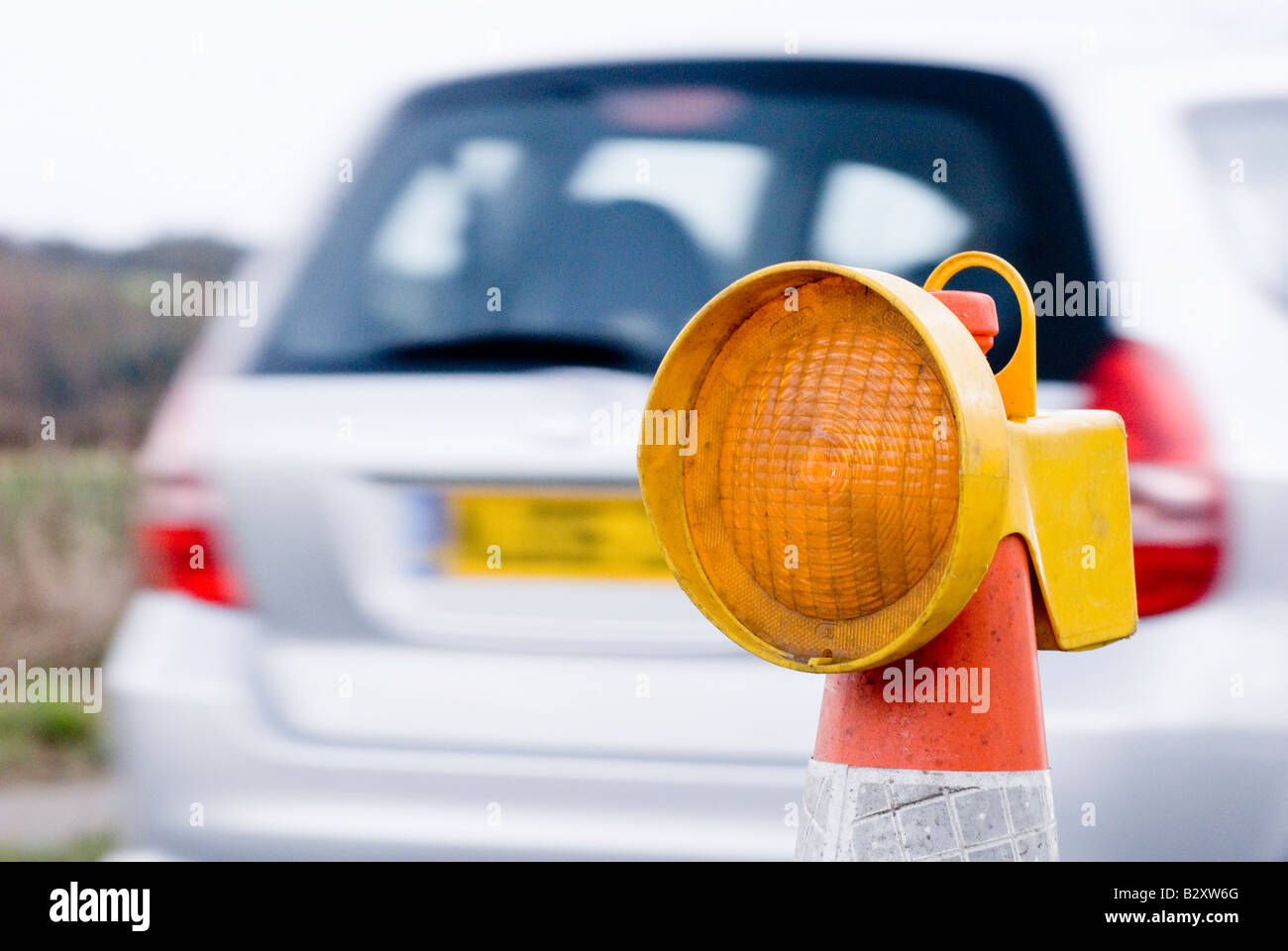 car passing a yellow flashing light on top of a cone in roadworks in
