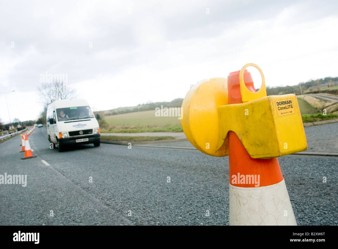 Van passing a yellow flashing light on top of a cone in roadworks in the uk Stock Photo