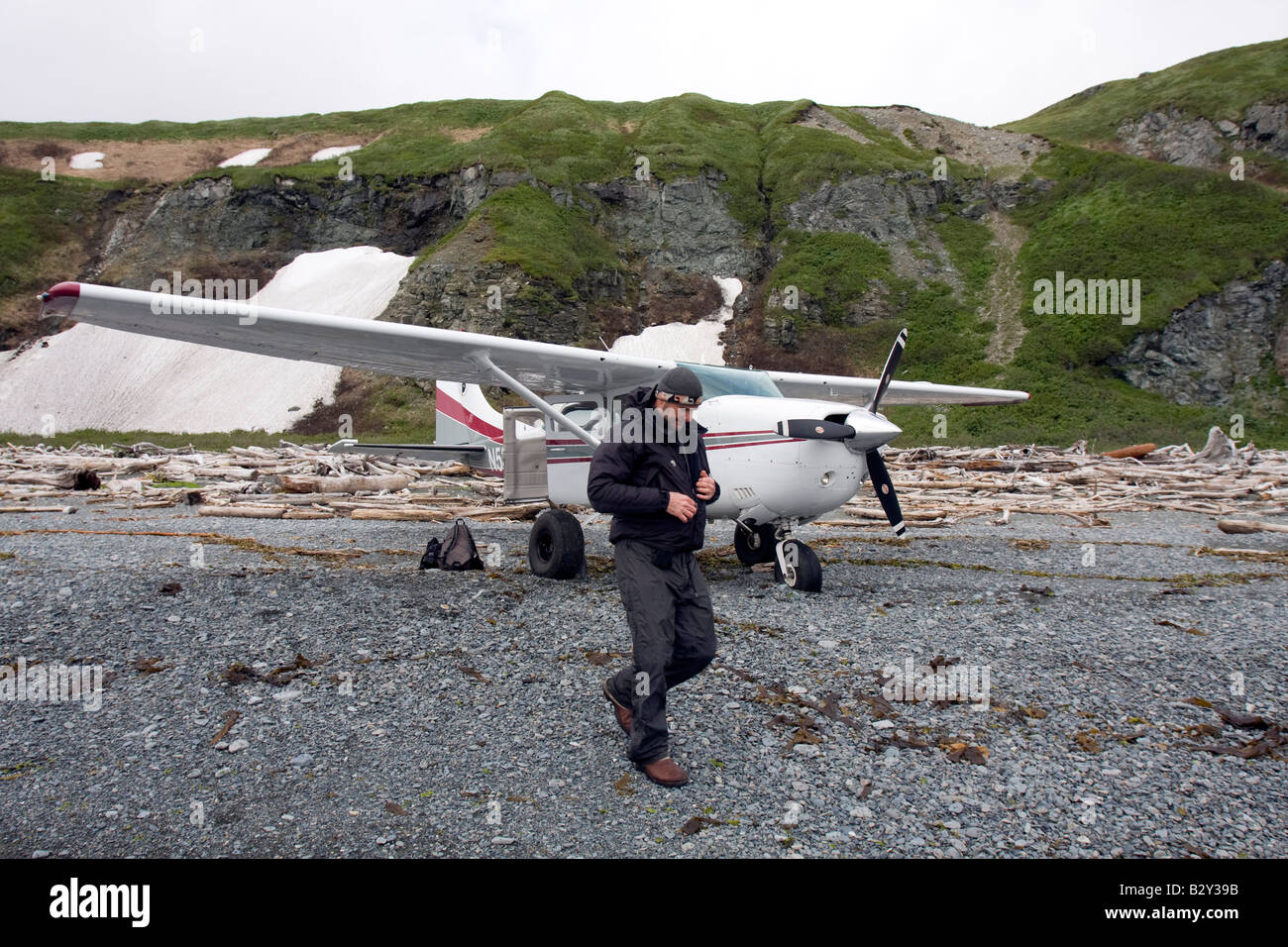 Pilot in front of his airplane on a driftwood covered beach in Katmai National Park and Preserve, Alaska, US Stock Photo