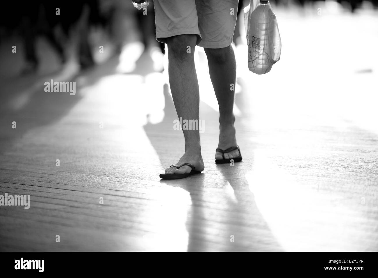 Mans walking along on a hot summers day carring a bottle of water wearing flip flops Stock Photo