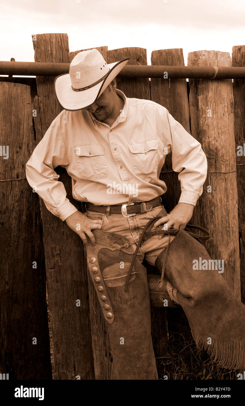 The life of a cowboy in the West USA as cowboy relaxes by ranch in jeans and chaps Stock Photo