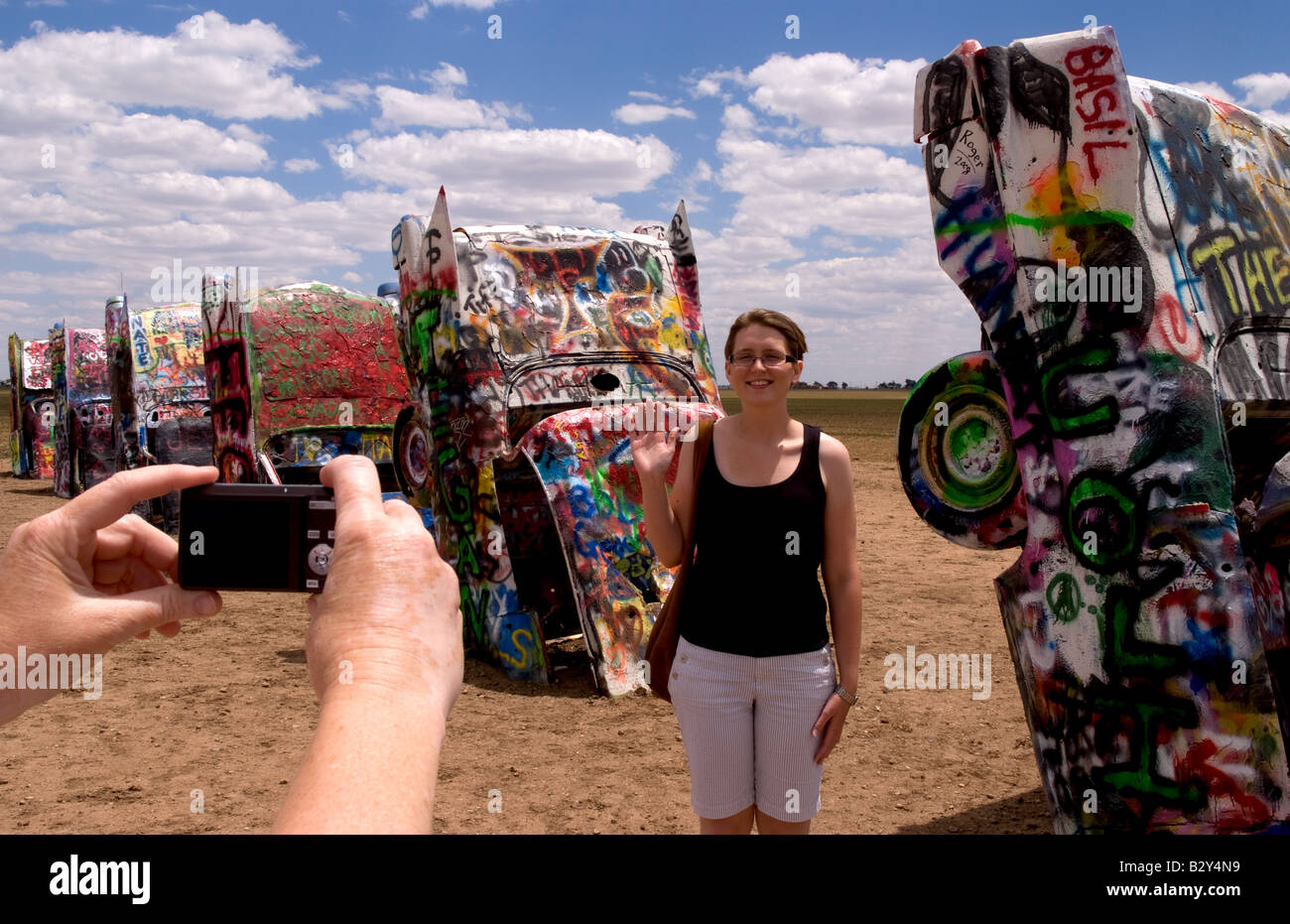 Tourist taking picture with camera at the Cadillac Ranch with buried cars in ground in Amarillo Texas USA Stock Photo