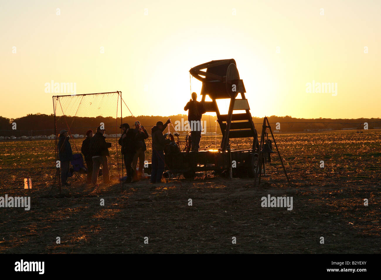 Wooden barrel human powered pumpkin flinging machine with people pulling down the flinging arm silloutted against setting sun Stock Photo