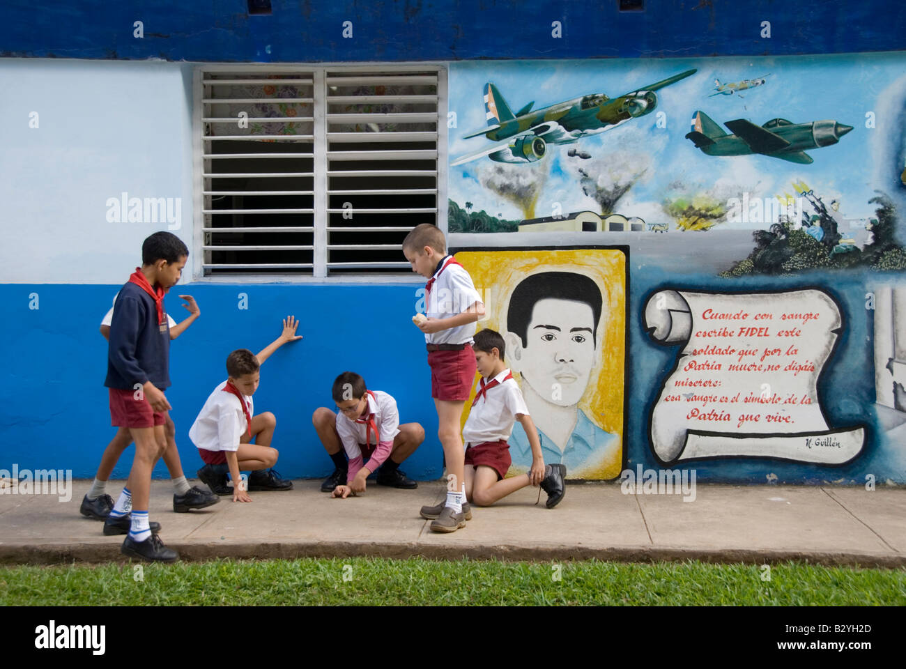 School children playing in playground beside socialist propaganda mural paintings Viñales Cuba Stock Photo